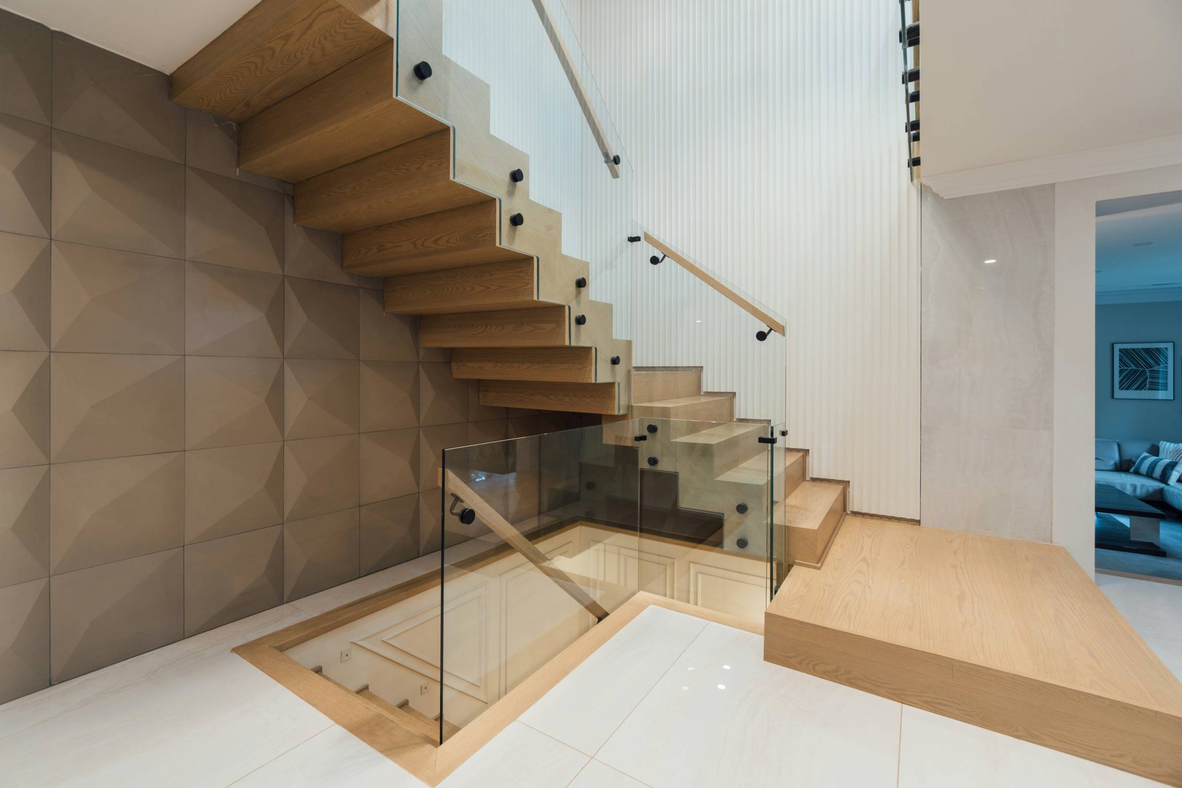 Oak floating stair turning at a landing, with clear frameless glass railing panels and a wall-mounted handrail