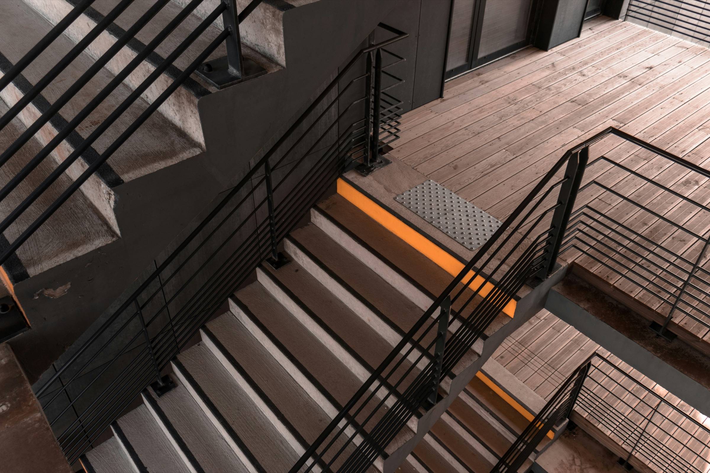 Black horizontal-bar metal railing following a stair down to a wood deck, seen from above