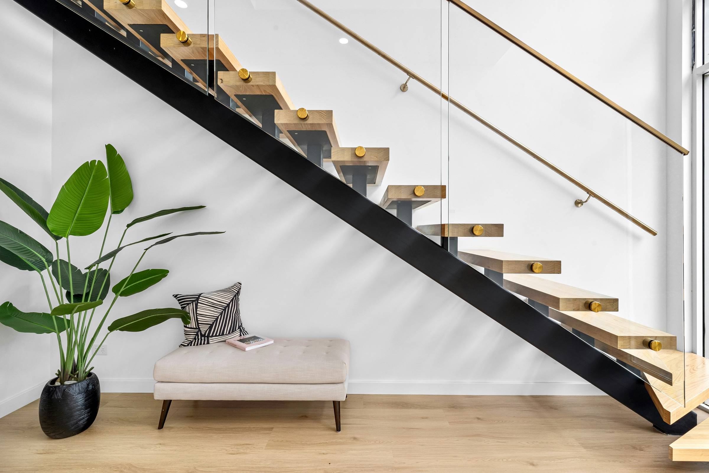 Floating stair with a black steel mono-stringer, oak treads, and a slim wall-mounted handrail in a bright living space