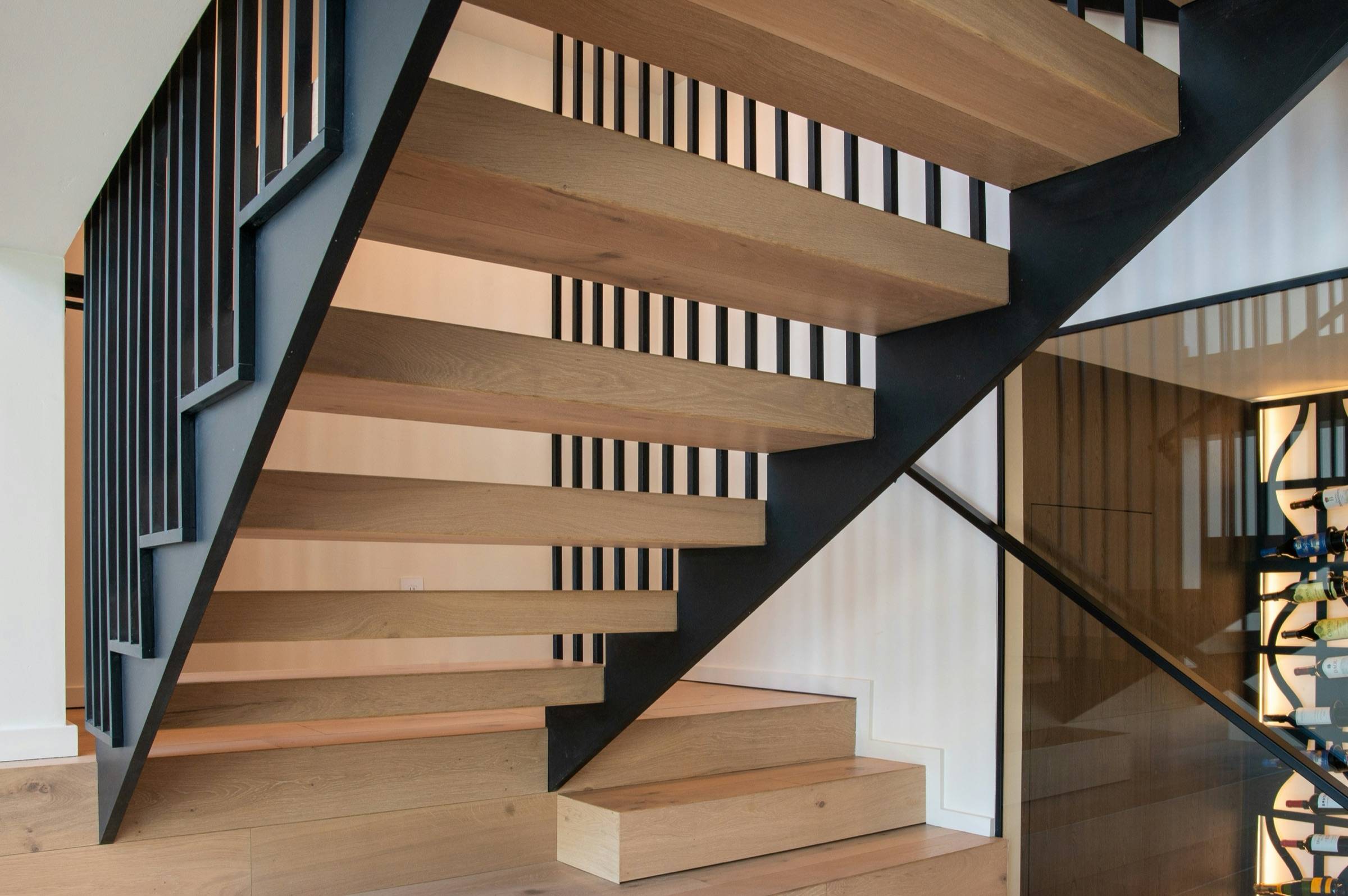 Black steel stringer stair with light wood treads and a vertical black picket guard in a bright interior