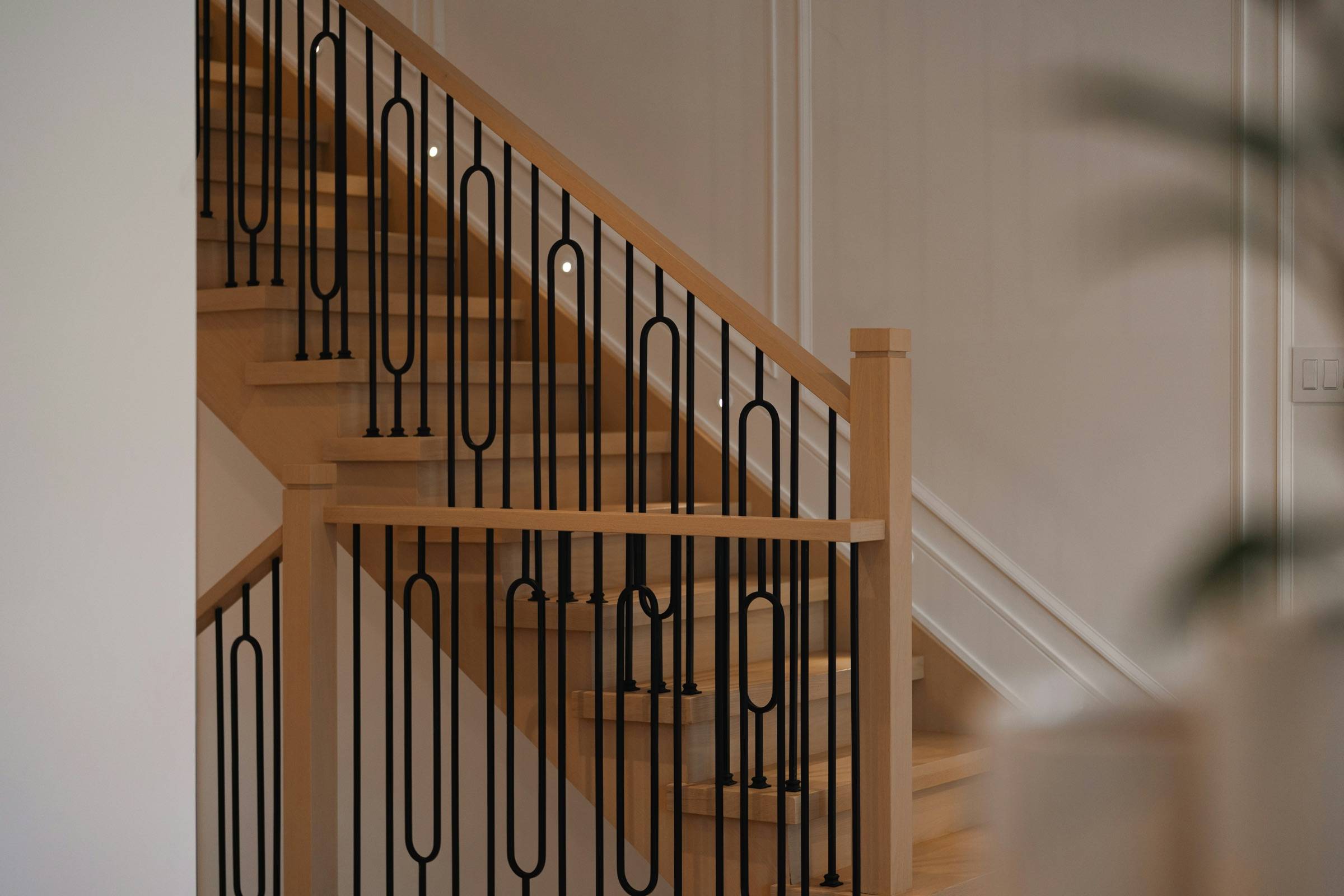Close view of a stained-oak stair with black wrought-iron balusters in a looped pattern and a wood handrail